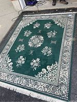 Full view of green and white floral patterned area rug laid flat on pavement, showing color and overall condition.