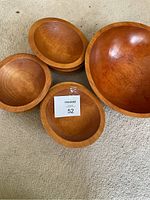 Five wooden bowls arranged on beige carpet, showing various sizes including smaller and larger bowls.
