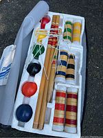 Overview of the croquet set contents in white foam tray, showing six colored wooden balls, six wooden mallets with striped grips, metal wickets, and stakes.