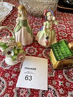 Two Doulton figurines, porcelain flower basket and Japanese style container arranged on a patterned fabric background