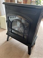 Front view of black electric fireplace heater with decorative glass door and legs.