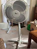 Full view of the white Super brand adjustable oscillating floor fan on the carpeted floor showing base, pole, and head position.