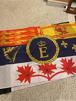 Flag with Royal Canadian Navy emblem and Canadian maple leaf in red, yellow, blue, and white colors laid flat on carpet.