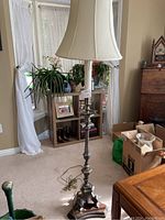 Full view of the floor lamp showing the wooden base, pewter shaft, and white bell-shaped lampshade standing in a room.