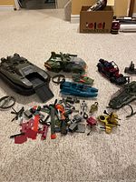 Overview showing multiple GI Joe vehicles including hovercraft, armored vehicle, helicopter, jeep, figures and accessories scattered on floor