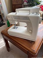 Full side view of white Kenmore sewing machine on wooden table, carrying case visible in background.