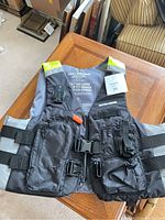 Front view of Seadoo life jacket showing pockets, whistle, buckle, and zipper on wooden table.