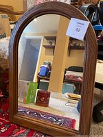 Full front view of the wood framed arch top mirror leaning against a table, showing the reflective surface and frame details.