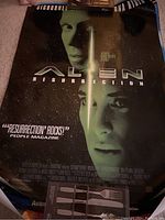 Alien Resurrection movie poster showing faces of Sigourney Weaver and another character, dark green and black background, 'Resurrection Rocks!' text visible