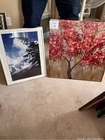 Two nature prints shown side by side on the floor. Left print features a photographic image of a pine tree and snowy mountains. Right print features a painting of a tree with red blossoms.