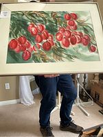 Framed watercolour painting showing red berries on leafy branches, held by person to display size, includes white matte and frame without glass.