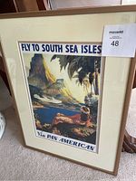 Photo of the framed Pan American Airways poster showing the tropical island scene with the seaplane and reclining woman, including visible MaxSold tag.