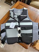 Front view of the grey and black Seadoo life jacket showing zipper and buckle closures on a wooden table.