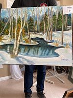 Full view of the oil painting held by a person showing the entire canvas depicting a snowy stream and trees.