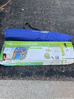 Photo of boxed badminton and volleyball combo set along with blue portable sun shade in bag on pavement
