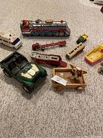 Wide view of diverse vintage toys on carpet, showing tin train, toy vehicles, and wooden cart.