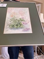 Framed watercolour floral painting with green matte held by person showing full framed artwork.