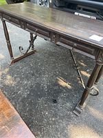 Full front and side view of wooden desk top with three drawers and wrought iron legs and supports.