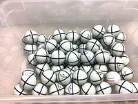 Top-down view showing a clear plastic bin containing approximately 50 white Callaway golf balls, each marked with multiple black alignment lines forming crosses.