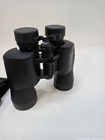 Black Bushnell 20x50 binoculars showing front and top sides. Lens covers are on eyepieces but front lens covers missing.