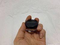 Hand holding a small round container of Bare Minerals Mini Eye Color with black lid showing brand name.