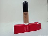Photo of the Shiseido Synchro Skin Glow foundation bottle with black pump on top and red packaging box lying horizontally beneath it.
