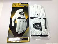Top view of golf glove in retail packaging, displaying front side of glove and black Callaway logo on white synthetic leather.