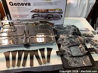SWISSMAR Geneva Raclette Party Grill unit with heating element and frame, eight raclette pans and eight spatulas laid out, original packaging box behind the grill.