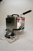 Side view of the T-fal stainless steel deep fryer with attached handle, power cord, and buttons. Original manual included for reference.