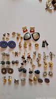 Top down photo showing all 27 pairs of vintage earrings in various designs, sizes, and materials laid out on a white surface.
