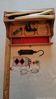 Photo showing entire collection: wooden glove stretchers, wooden smokers cabinet with red felt lining, wooden pipe, Swiss army tool, metal fish scale, early eyeglasses, and beadwork pieces laid out on flat surface.