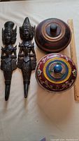 Two carved Dewi Indonesian wall figures alongside two carved wooden bowls with lids and a ruler for scale