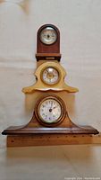 Three small antique mantel clocks stacked with a measuring ruler alongside, showcasing their size and condition.