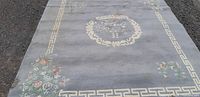Full view of the Indian wool carpet showing its overall design with a central floral medallion and floral corners on a grayish background with Greek key border.