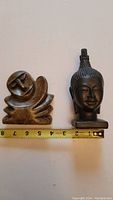 Photo showing both sculptures side by side with a ruler indicating size. The stylized human figure is about 4.5 inches tall, the Buddha head about 4 inches tall.