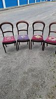 Full view of four Victorian-style chairs in a row showing wood frames and needlepoint upholstery.