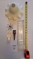 Top-down view of the four items in the lot: milk glass lamp shade, Swarovski crystal flower, silver wine funnel, and clear glass tray, with measuring tape for scale