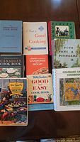 Display of 9 vintage cookbooks laid out flat on a table showing various titles and cover designs.