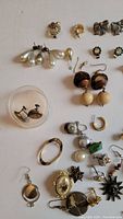 Close-up image showing assorted earrings including pearl drops, clip-ons, gold-tone pieces, and various pins