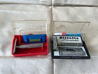 Top-down photo of the two vintage Gillette razors each in their open original plastic cases showing metal razors, blue blades, brush, and labels