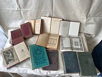 Overview photo of 13 antique books with various covers and several open to show pages and inscriptions.