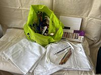 Overview photo of all art supplies in and around green and white reusable bags, including canvases, paint, pencils, and painting tools.