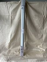 Full view of the rolled blackout blind in protective plastic packaging, upright against a fabric backdrop.