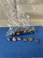 Photo of six metal enamel lapel pins with checkered flag designs in various colors and patterns, displayed on a blue surface with a clear plastic bag behind them.