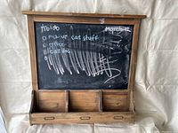Front view of wood framed chalkboard with visible chalk markings and three storage compartments below the chalkboard surface.