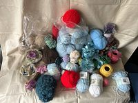 A large collection of assorted yarn balls, skeins, and bundles in various colors and textures arranged on a beige fabric background.