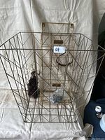 Photo of a large wireframe metal rolling laundry basket along with a matching wire wall mount rack. Inside the laundry basket is a black cloth or bag and a small plastic bag with hardware.