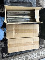 Three cardboard boxes, two closed and one opened containing metal drawer slides hardware arranged vertically inside.