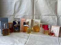 Full view of eleven vintage perfume bottles with original boxes lined up side by side on a white fabric background
