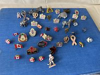 Photo of assorted vintage pins laid out on a blue surface showing details and variety of the pins.